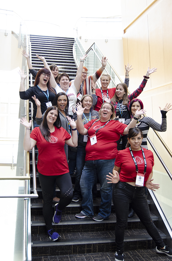 A group of 12 women posed on a staircase, hands raised in celebration for the photo. Ladies of WordPress - Photo by David Needham